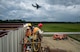 A Charleston C-17 Globemaster III approaches to land June 27 while  Staff Sgt. Martin Lilland, 556th RED HORSE at Hurlburt Field, Florida, and Senior Airman Darrien Anderson, 560th RED HORSE Squadron Joint Base Charleston, South Carolina, position their lift to hang insulation and panels on a 4,800 square-foot preengineered  building building to store RED HORSE construction equipment and gear.  Rapid Engineer Deployable, Heavy Operational Repair Squadron, Engineer (RED HORSE) squadrons provide the Air Force with a highly mobile civil engineering capability in support of contingency and special operations worldwide. They are self-sufficient, mobile squadrons that provide heavy construction support such as runway/facility construction, electrical upgrades, and equipment transport when requirements exceed normal base civil engineer capabilities and where Army engineer support is not readily available. (U.S. Air Force Photo by Michael Dukes)