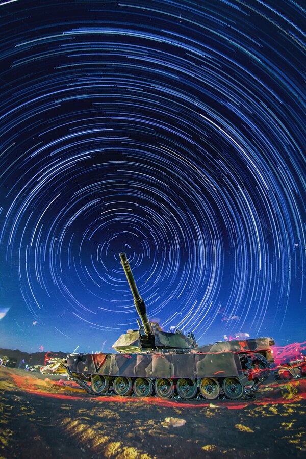 An M1-A1 Abrams tank is staged in preparation for the culminating event during the 11th Marine Expeditionary Unit’s Combined Arms Exercise 2016 at Marine Corps Air Ground Combat Center Twentynine Palms, Calif., 16 June. Timed exposures of the night sky produce an effect referred to as ‘star trails’; the movement of the earth makes the exposure of the stars like that of a moving object, producing lines or circles of light. The blurred red lighting in the photograph is the same effect, but that of Marines on fire watch, walking by the tank with a red-lensed flashlight. Combined arms is the full integration of available fire power such as close-air support, indirect fire by mortars or artillery, and ground troops’ weapons systems in such a way that to counteract one, the enemy must become vulnerable to another; it poses the enemy with a dilemma – a no-win situation.