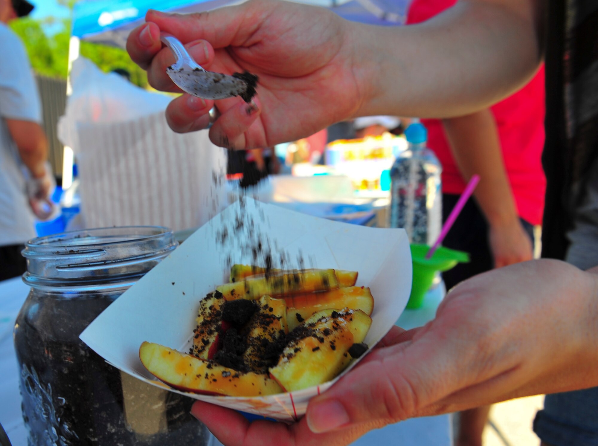A customer sprinkles cookie crumbs on a caramel apple from the Focus 5/6 group booth at the Sound of Independence on Hurlburt Field, Fla., June 24, 2016. Various squadrons and organizations on base provided attractions, as well as food and drinks, to Airmen and their families during the celebration. (U.S. Air Force photo by Airman Dennis Spain)