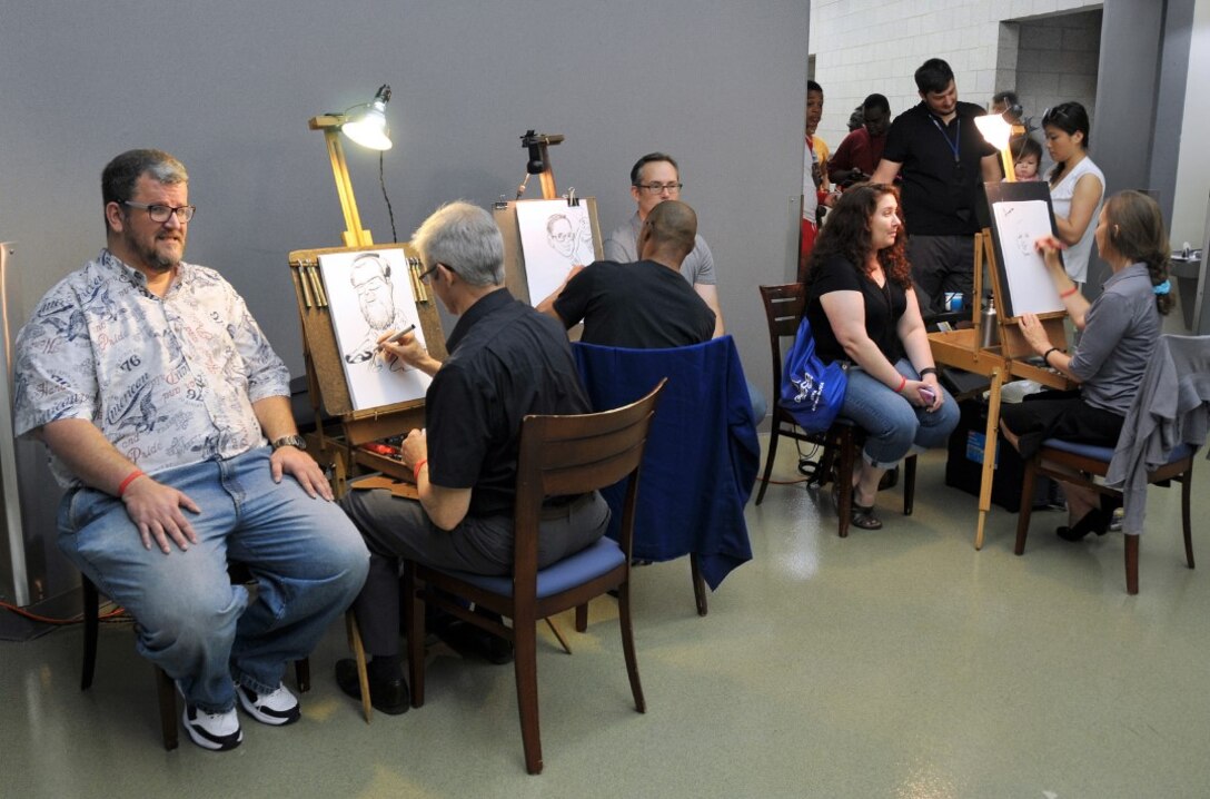 Employees and family members sit for their caricatures at the 2016 HQC Family Day at the McNamara Headquarters Complex at Fort Belvoir, Virginia, June 28.
