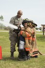 Airman 1st Class Leodanis Uceta, 5th Civil Engineer Squadron firefighter, helps Minot kids aim a hose during Heroes in Training at Minot Air Force Base, N.D., June 24, 2016. Heroes in Training is an event put on by the Minot AFB Fire Department to help show kids how first responders react to emergencies such as fires or accidents. (U.S. Air Force photo/Airman 1st Class Christian Sullivan)