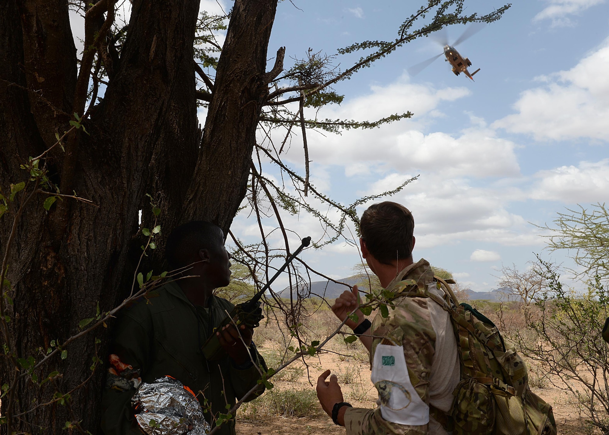 (From left) A Kenyan Defense Force airmen and U.S. Air Force Senior Airman Ian Khun, 82nd Expeditionary Rescue Squadron, survival evasion resistance and escape specialist, watch a helicopter during a hands-on scenario for African Partnership Flight Kenya June 28, 2016 at Archers Post, Kenya.  The APF included a Kenyan-led exercise, Linda Rhino, in which instructors observed the application of what was learned in the classroom and provided feedback. The exercise included multiple personnel recovery scenarios. (U.S. Air Force photo by Tech. Sgt. Evelyn Chavez/Released)