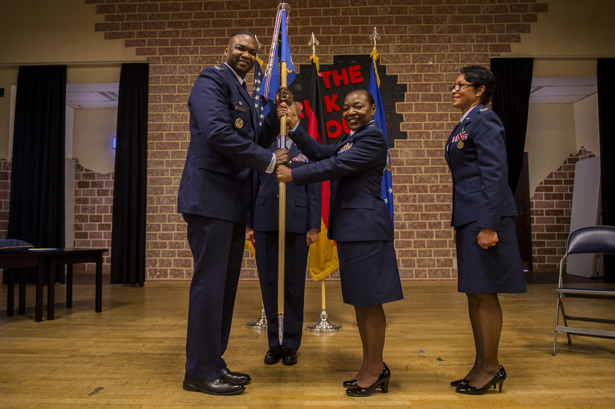 U.S. Air Force Col. Alfred Flowers, 52nd Medical Group commander, left, passes the 52nd Medical Operations Squadron guidon to U.S. Air Force Lt. Col. Rebecca Elliott, 52nd MDOS commander, center, while U.S. Air Force Col. Patricia John, former 52nd MDOS commander, watches during the 52nd MDOS change of command ceremony at the Brickhouse on Spangdahlem Air Base, Germany, June 29, 2016. The passing of the guidon is a military tradition when changing command. (U.S. Air Force photo by Senior Airman Luke Kitterman/Released) 
