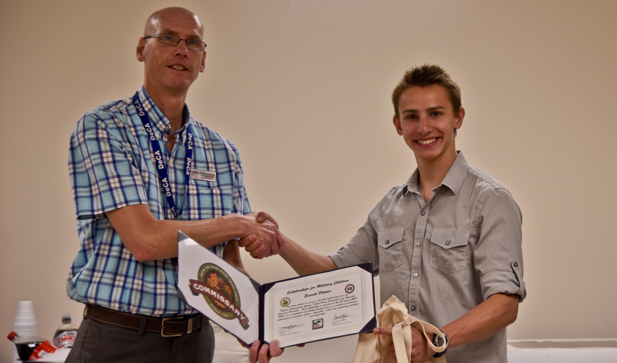 Eric Quantock, Fairchild Commissary store director, gives a certificate to Everett Plotner, student, during a ceremony June 29, 2016, at Fairchild Air Force Base, Wash. Plotner was one of five military children to win a $2,000 scholarship given out by the Defense Commissary Agency. He is a high school senior planning to attend college in the fall. (U.S. Air Force photo/Airman 1st Class Taylor Shelton)