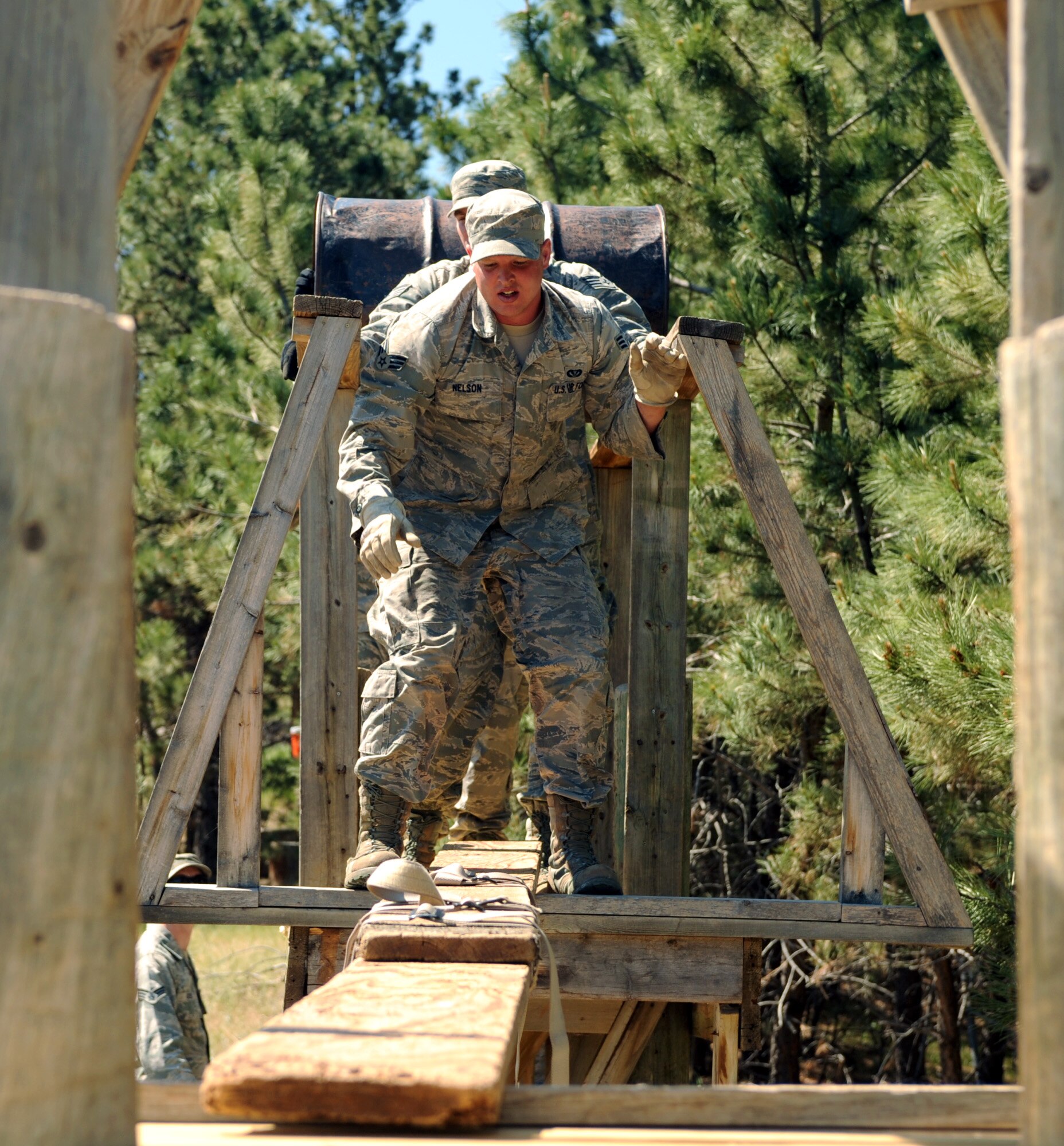 Senior Airman Kurt Nelson, 28th Civil Engineer Squadron structures apprentice, prepares to cross a make-shift bridge during a leadership reaction course at the South Dakota National Guard West Camp Rapid training facility, Rapid City, S.D., June 17, 2016. The purpose of this obstacle was to move all the materials given from one side to another without dropping any of them on the ground below them in 20 minutes. (U.S. Air Force photo by Airman 1st Class Denise M. Nevins/Released)