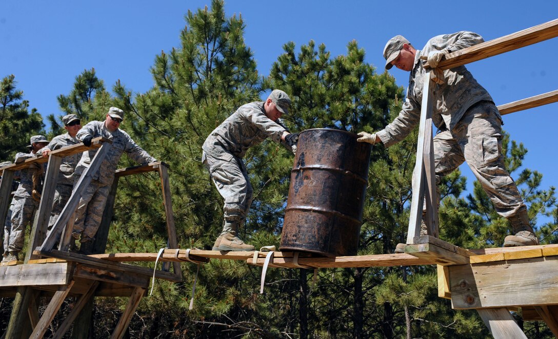 Staff Sgt. David Loving, 28th Civil Engineer Squadron structures apprentice, center, prepares to pass an oil drum to Senior Airman Kurt Nelson, 28th CES structures apprentice during a leadership reaction course at the South Dakota National Guard West Camp Rapid training facility, Rapid City, S.D., June 17, 2016. The course included over 10 different obstacles designed to build and strengthen team cohesion and communication skills. (U.S. Air Force photo by Airman 1st Class Denise M. Nevins/Released)