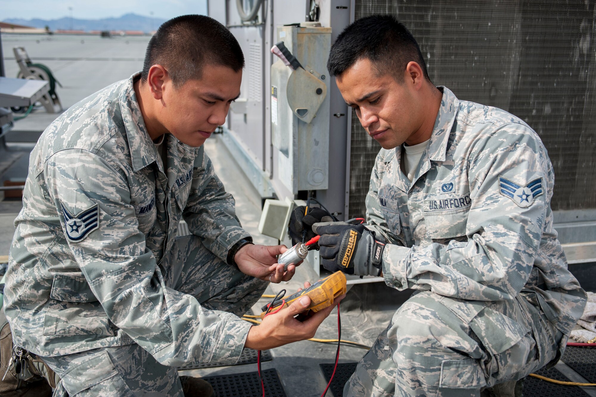 Staff Sgt. Dads Zyron Maniego, 99th Civil Engineer Squadron Heating, Ventilating, and Air Conditioning technician, and Senior Airman Octavio Nila 99th CES HVAC technician, check readings on a part used for an A/C unit atop of the Base Exchange on Nellis Air Force Base, Nev., June 28, 2016. After receiving 112 emergency calls last week, HVAC were able to fix and reset each unit atop of the BX within a 24 hour time frame.