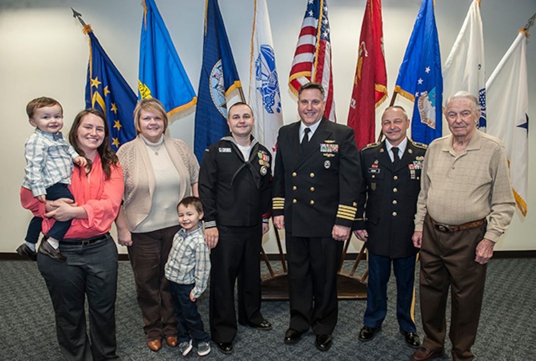Petty Officer 2nd Class Anthony Brown (fourth from left) reenlisted for eight more years in the Navy. Pictured with him is (l-r) wife, Deisree, son Grant, his mother Anthony and son Carter, U.S. Navy Capt. Justin Debord, DLA Land and Maritime Chief of Staff, father Karl and grandfather Karl Sr. 