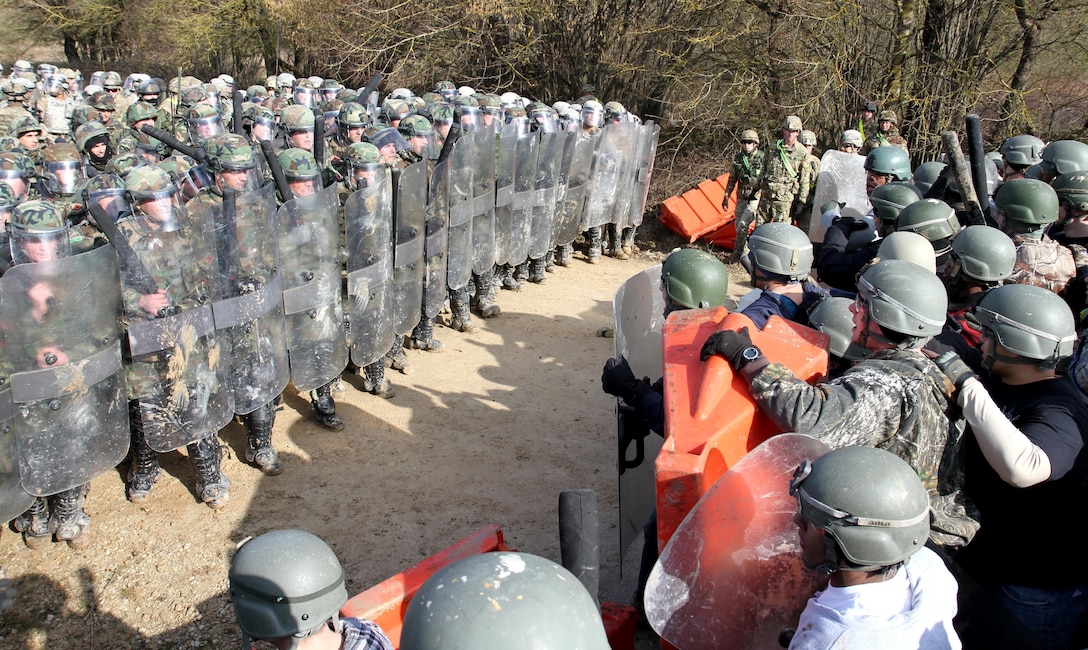 U.S. soldiers, left, await further instructions before engaging mock protesters during crowd control training at the Joint Multinational Readiness Center in Hohenfels, Germany, Feb. 25, 2016. Army photo by Staff Sgt. Thomas Duval