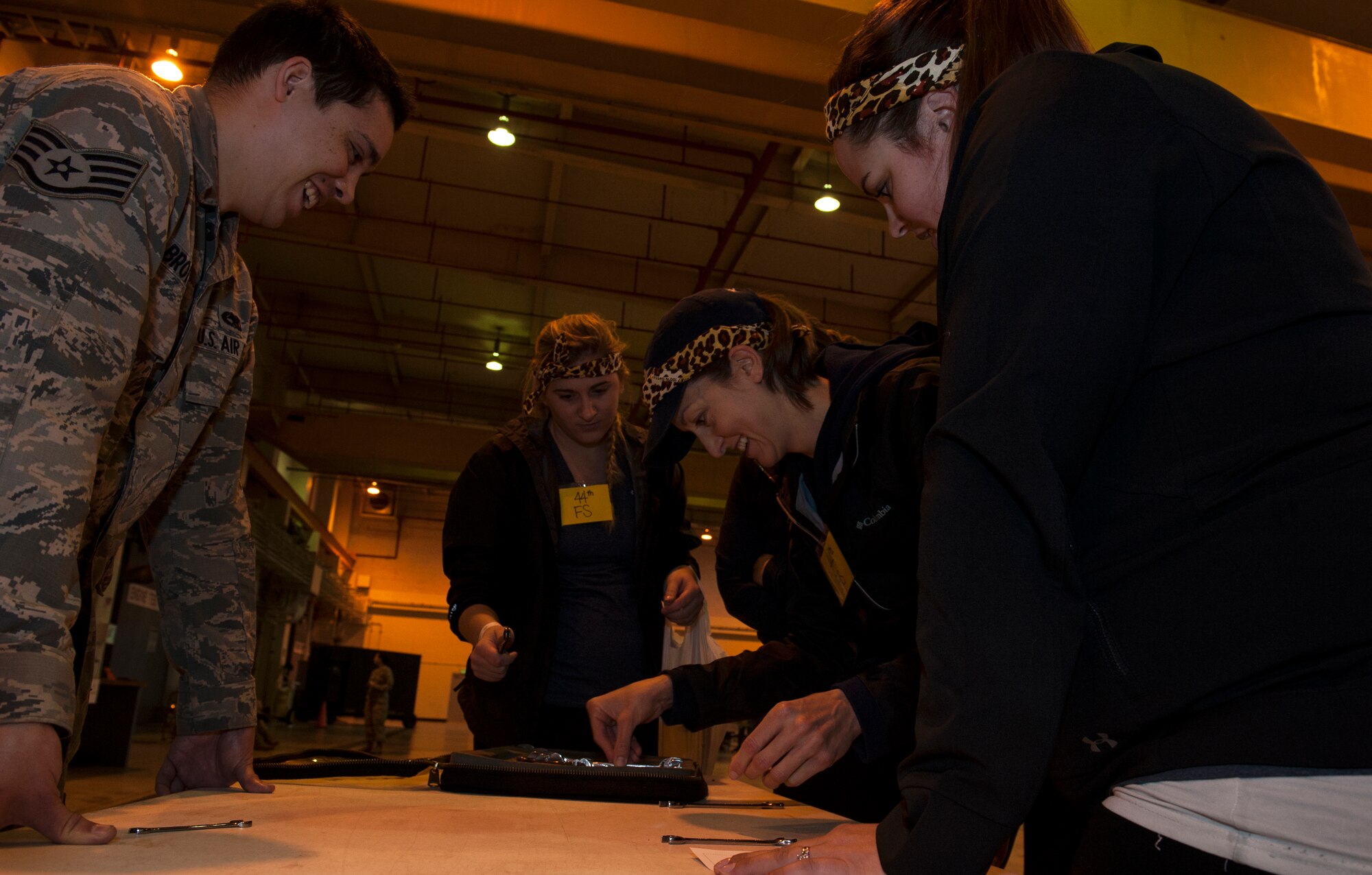 U.S. Air Force Staff Sgt. Kyle Brotherton, 18th Component Maintenance Squadron F-15 Eagle crew chief, assists spouses from the 44th Fighter Squadron with a challenge during Team Kadena Spouses’ Amazing Race Feb. 24, 2016, at Kadena Air Base, Japan. During this particular challenge, team members had to arrange a set of tools correctly and find a tool that was incorrectly labeled. (U.S. Air Force photo by Airman 1st Class Lynette M. Rolen)