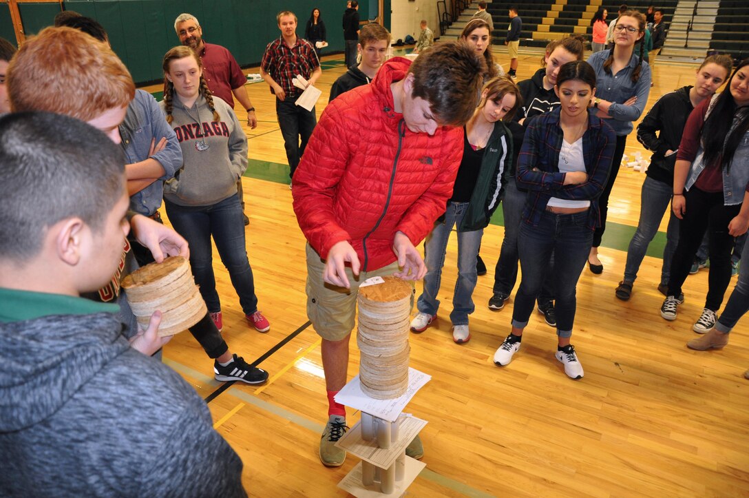 DeSales High School freshman Jake Wylie applies weights to his team's paper tower  while other participants look on.