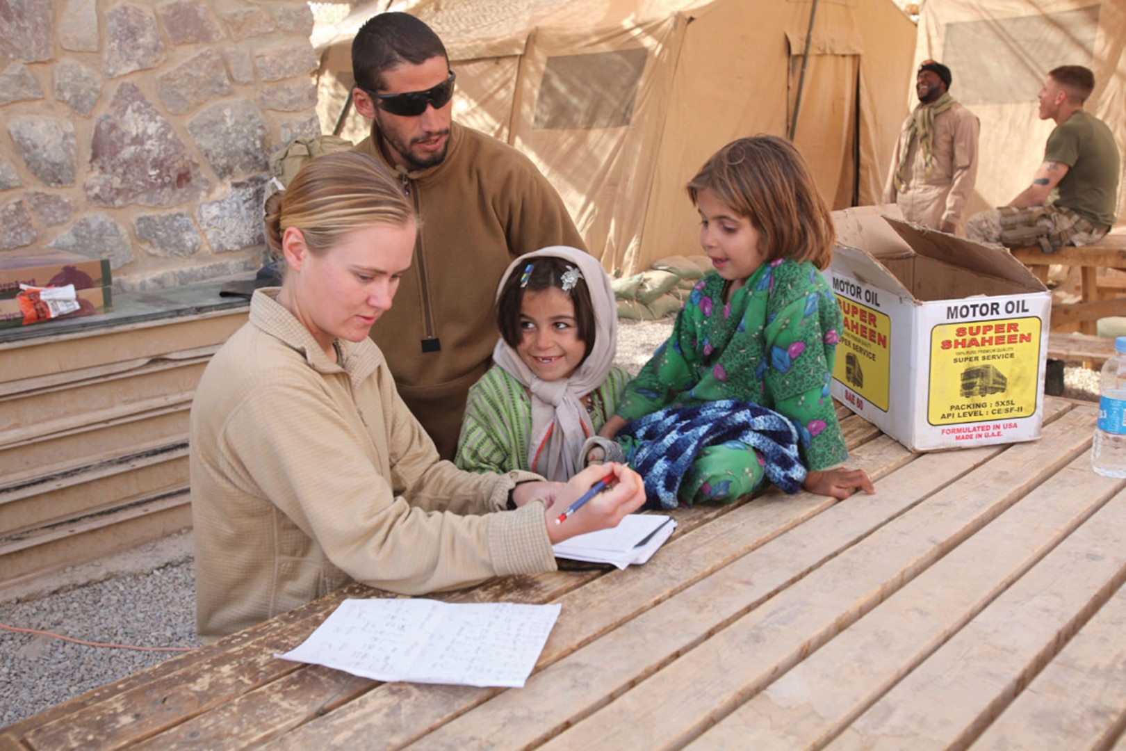 A U.S. Army Staff Sergeant, with the aid of an interpreter, helps two local Afghan girls practice reading and spelling.