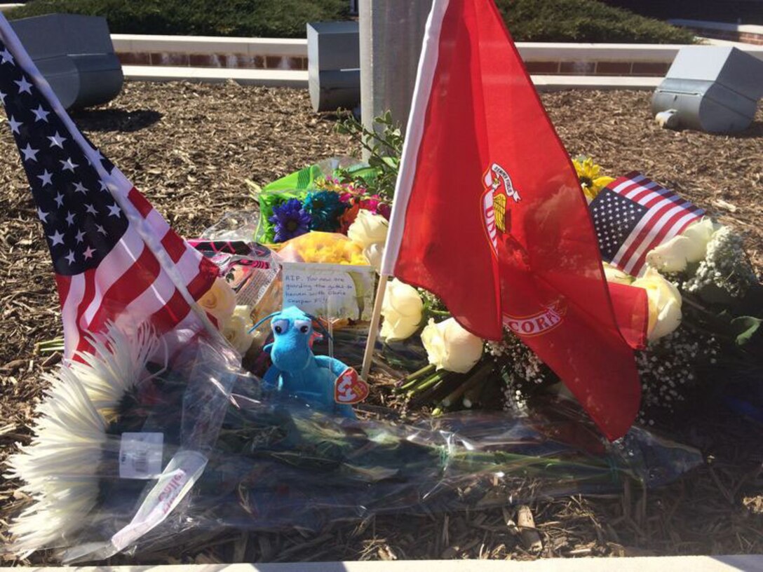 Flowers, the U.S. and Marine Corps flags and a blue stuffed dragon are among the items of remembrance at PWPD. The stuffed blue dragon is affixed with a hand-written note: "RIP. You are now guarding the gates of heaven with Chris. Se per Fi."
