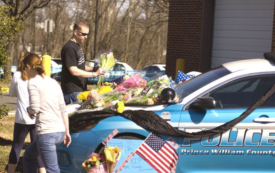 Greg, a member of an area agency who would not provide his last name, lays flowers on a makeshift memorial for Prince William Police Officer Ashley Guindon who was shot to death Saturday evening in Woodbridge. Two of her colleagues were wounded. The officers were called to a domestic disturbance at a house on Lashmere Court. The body of a woman was found at the house. 