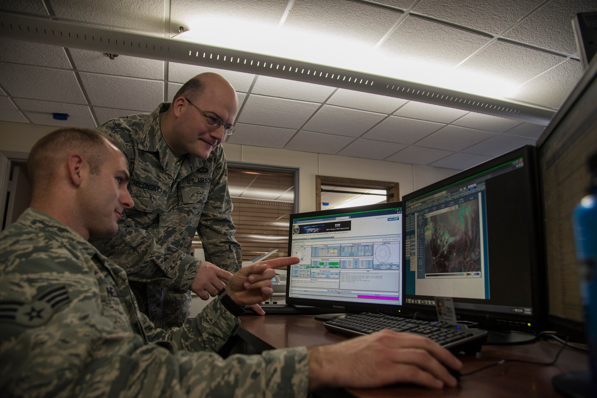 Master Sgt. Timothy Yablonsky, 15th Weather Squadron standards and evaluations NCO in charge, discusses what weather conditions are forming inside their area of responsibility with one of his Airmen Feb 29, 2016 at Scott Air Force Base, Ill. Yablonsky aided in the rescue of a Belleville, Illinois, family when their home was caught on fire. (U.S. Air Force photo/Senior Airman Jake Eckhardt)
