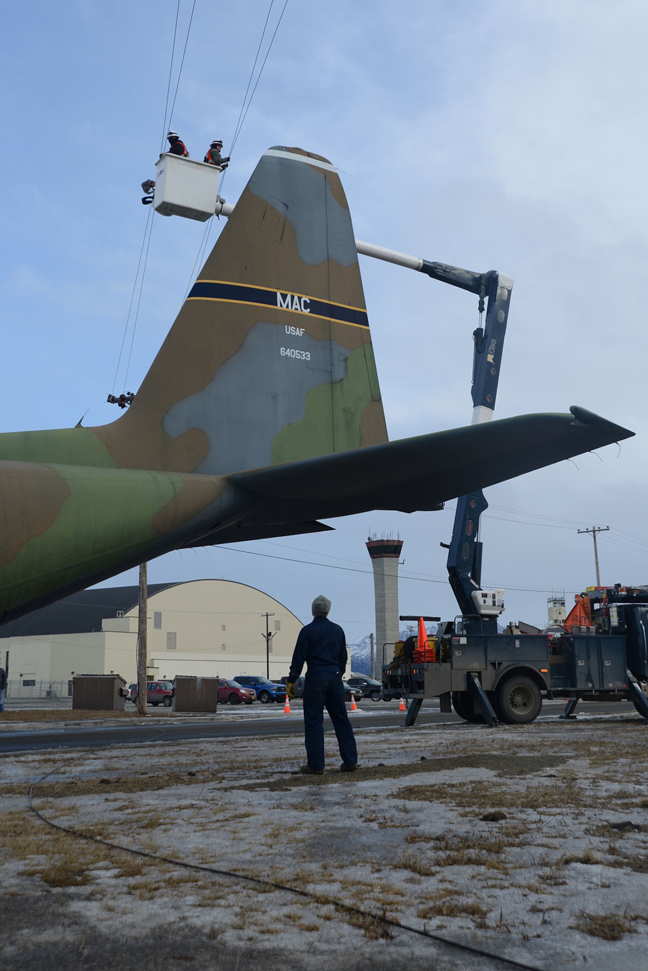 Contracted personnel with General Communications Inc. lift power lines out of the way during the static C-130 Hercules movement at Joint Base Elmendorf-Richardson Feb. 27, 2016. Due to the height of the aircraft some power lines were removed and others were lifted for minimal damage. (U.S. Air Force photo by Airman 1st Class Christopher R. Morales)