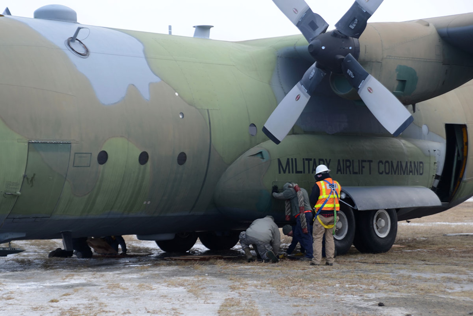 Airmen and contracted personnel work together to tow the static C-130 Hercules at Joint Base Elmendorf-Richardson Feb. 27, 2016. Dirt and wooden planks were laid down in front of the aircraft’s wheels to prevent getting stuck as it is relocated to Hangar 21 for refurbishment. (U.S. Air Force photo by Airman 1st Class Christopher R. Morales)