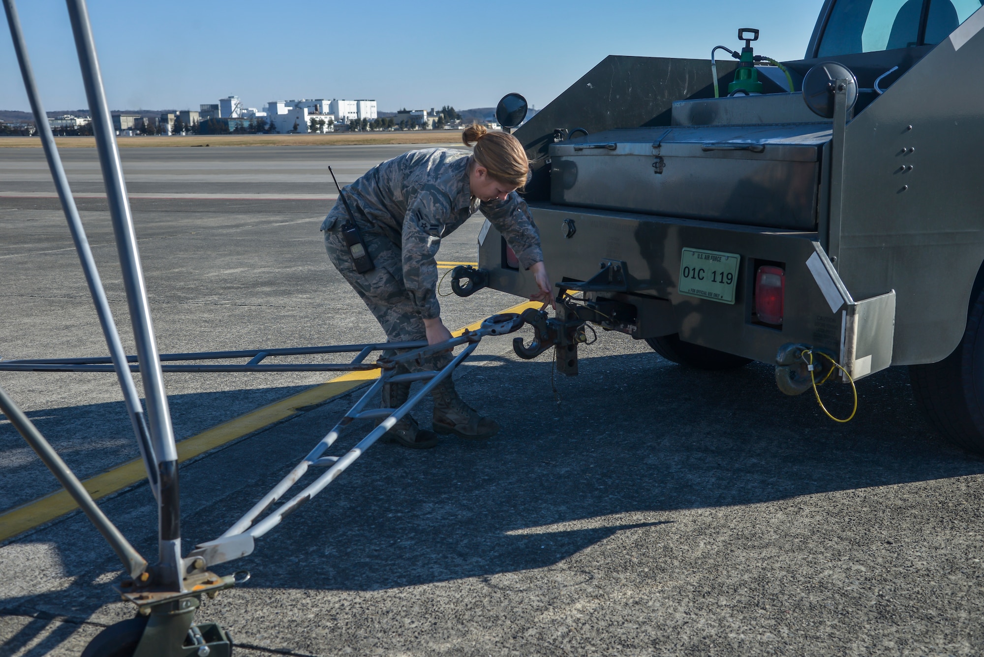 Airman 1st Class Abigail Kuras, 374th Maintenance Squadron Aerospace Ground Equipment apprentice, hooks a stand onto a vehicle to tow it to the stand storage area at Yokota Air Base, Japan, Feb. 11, 2016. The AGE flight uses bobtail tow vehicles, a scooter, and electric warehouse tugs to accomplish daily mission requirements. (U.S. Air Force photo by Senior Airman David Owsianka/Released)