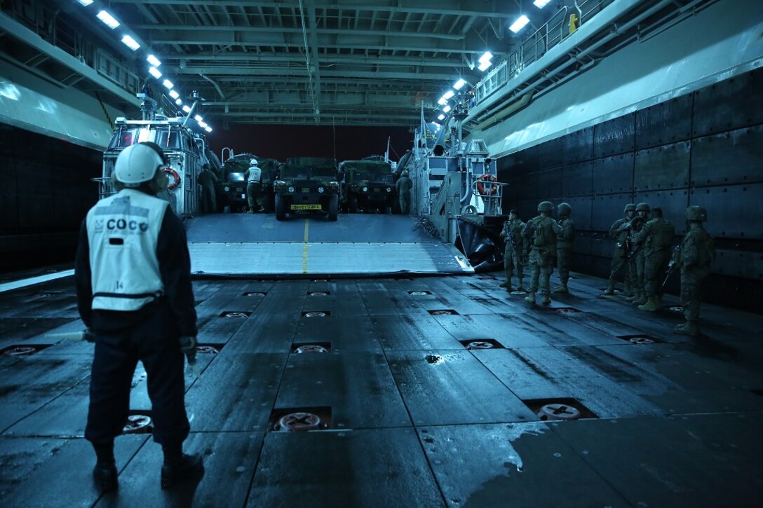 A well deck crew member aboard the USS Essex (LHD 2) waits to guide High Mobility Multipurpose Wheeled Vehicles off a Landing Craft Air Cushion to the cargo hull of the ship near Camp Pendleton Feb. 22, 2016. The vehicles were the first wave transported to the ship for the start of the Marine Corps Combat Readiness Evaluation of Company A, 3rd Assault Amphibian Battalion for their upcoming deployment. (U.S. Marine Corps photo by Lance Cpl. Timothy Valero/Released)