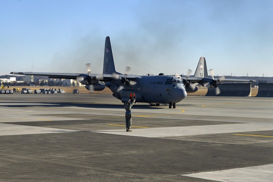An airman directs a C-130 Hercules aircraft onto the flightline on Yokota Air Base, Japan, March 2, 2016. The airman is a crew chief assigned to the 374th Aircraft Maintenance Squadron. Air Force photo by Senior Airman David Owsianka