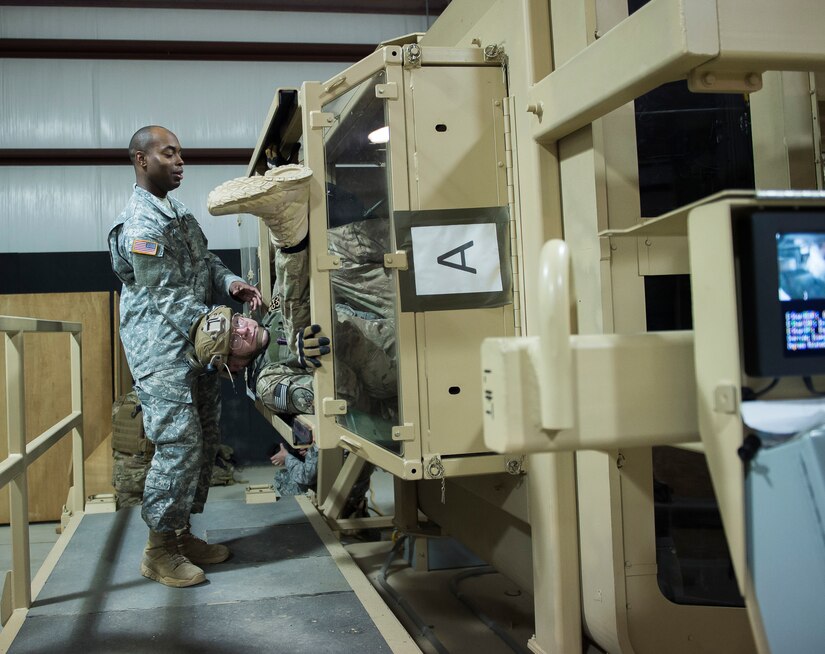 Sergeant 1st Class Ken Shirley, a High Mobility Multipurpose Wheeled Vehicle egress instructor at the McCrady Battle Simulation Center, assists a combat camera Airman March 3, 2016, during exercise Scorpion Lens 2016, at McCrady Training Center, Fort Jackson, South Carolina. The exercise is an annual training requirement incorporating combat camera job qualification standards and advanced weapons and tactical training with Army instructors. (U.S. Air Force photo/Staff Sgt. Jared Trimarchi)