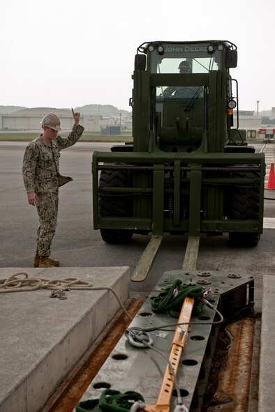 U.S. Navy Equipment Operator 2nd Class Joshua McDonald, Naval Mobile Construction Battalion 3 Seabees construction man, directs a forklift towards a fairlead beam on the flight line Feb. 29, 2016, at Kadena Air Base, Japan. Seabees utilized various heavy construction equipment to extract and replace an aircraft arresting barrier system. (U.S. Air Force photo by Senior Airman Peter Reft)