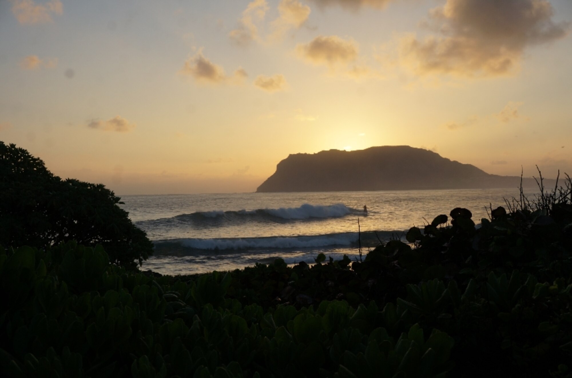 A lone surfer greets the sun as whale count volunteers assemble for a safety and accountability briefing at Marine Corps Base Hawaii's Pyramid Rock Feb. 27, 2016. Volunteers from the Air Force Installation Management Support Center's Detachment 2 have been supporting Sanctuary Ocean Count Site Leader, Capt. Natalie Chounet, for the early-morning ventures. The Sanctuary Ocean Count project is sponsored by the National Oceanic and Atmospheric Administration to provide scientists with data documenting the humpback whales’ annual 2,500-mile, round-trip migration from Alaska to the Hawaiian Islands. Chounet is the IMSC Det. 2 Basing and Beddown Flight’s deputy chief from Joint Base Pearl Harbor-Hickam, Hawaii. (U.S. Air Force Photo by Senior Master Sgt. Denise Johnson/released)