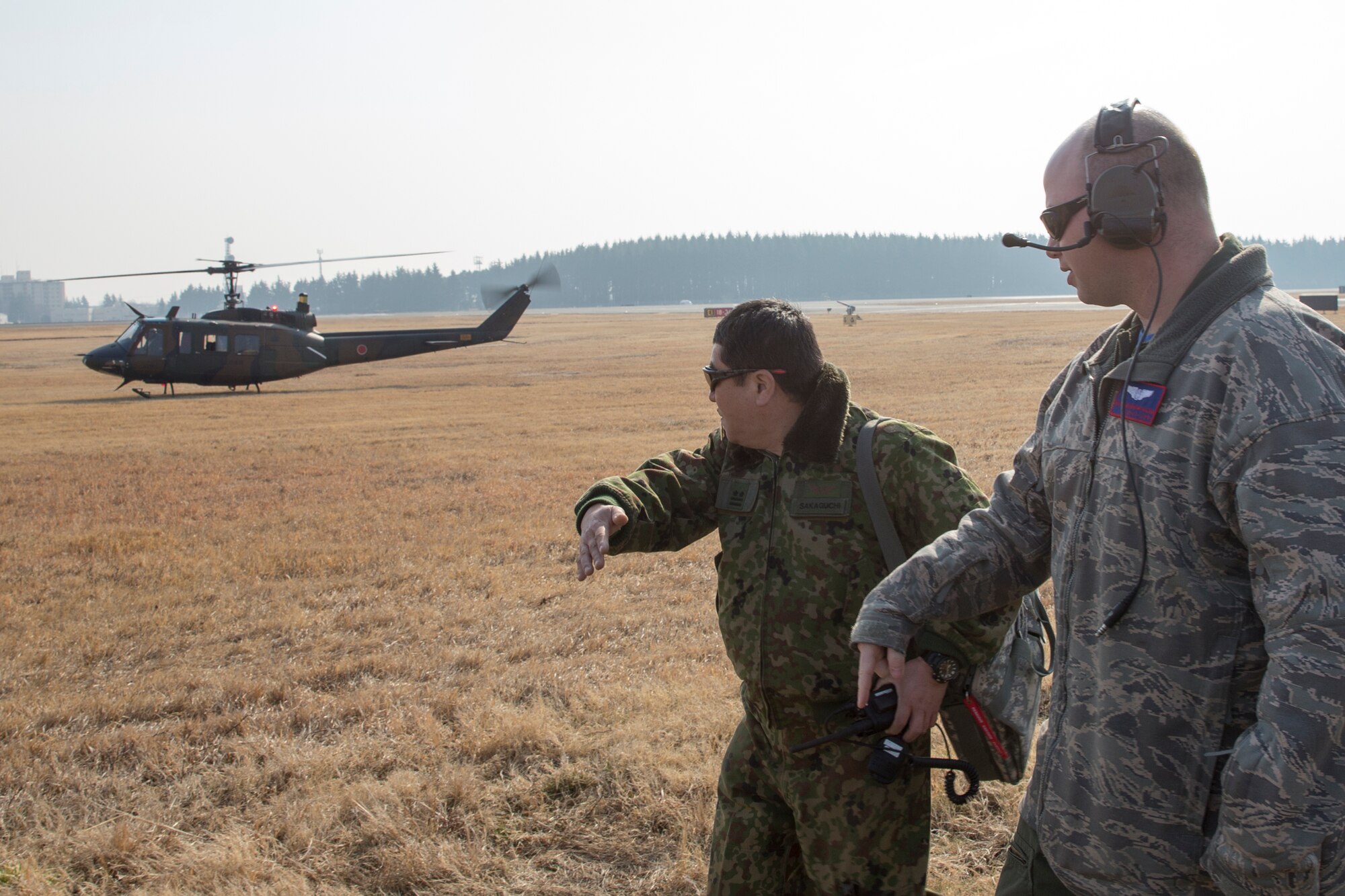 (Left and right) Japan Ground Self-Defense Force Lt. Col. Tatsuro Sakaguchi, Eastern Army Helicopter, 1st Aviation Unit executive officer, and U.S. Air Force Tech. Sgt. Christopher Rector, 459th Airlift Squadron UH-1N standardization, evaluation and flight engineer, walk on the flightline during search and rescue familiarization at Yokota Air Base, Japan, March 4, 2016. JGSDF members demonstrated their hoist capabilities to 459th Airlift Squadron members. (U.S. Air Force photo by Osakabe Yasuo/Released)