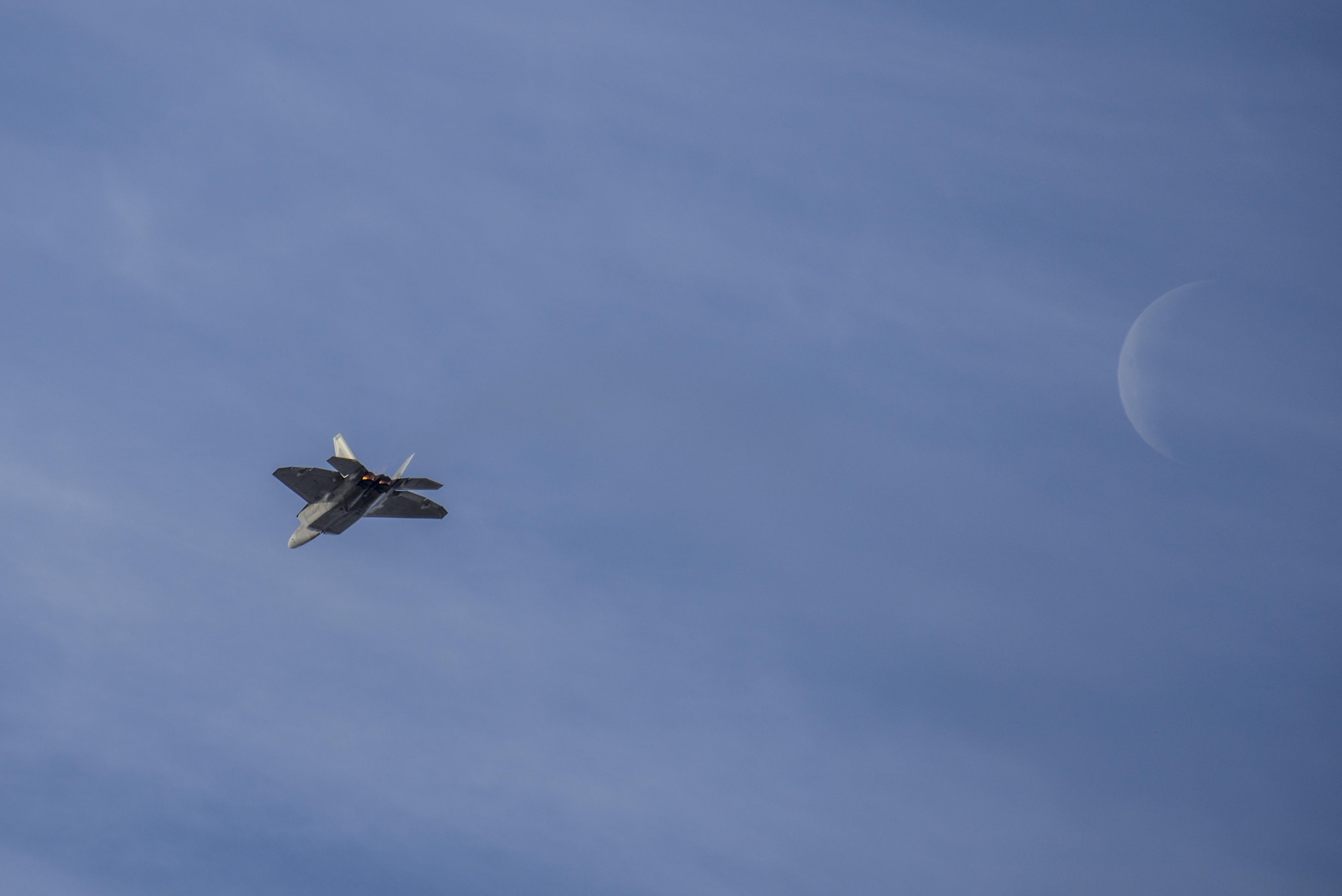 A U.S. Air Force F-22 Raptor flies in the foreground of the moon during the 2016 Heritage Flight Training and Certification Course at Davis-Monthan Air Force Base, Ariz., March 4, 2016. The annual aerial demonstration training event has been held at D-M since 2001 and features aerial demonstrations from historical and modern fighter aircraft. (U.S. Air Force photo by Senior Airman Chris Massey/Released) 