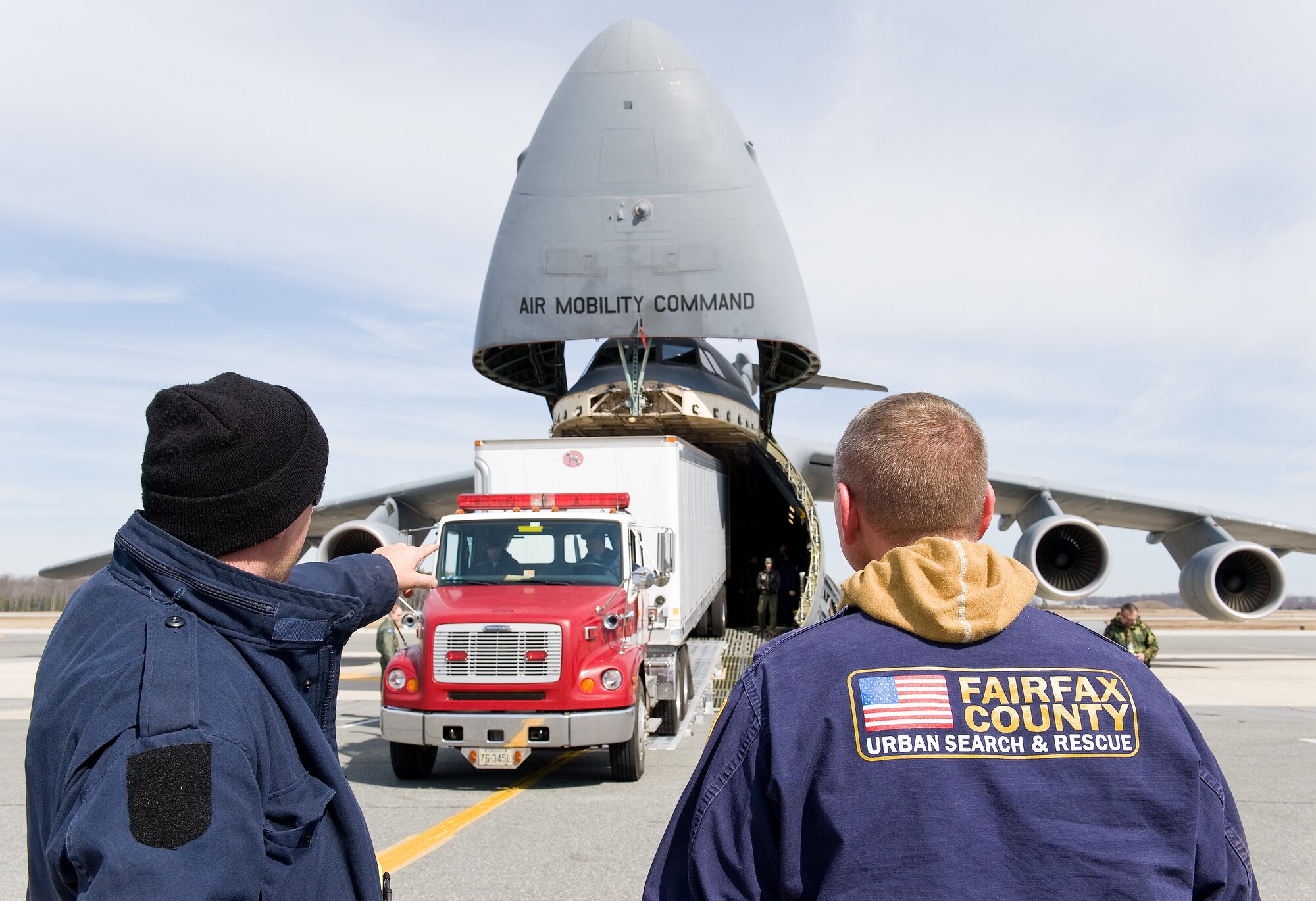 Archie Fellows, driver/mechanic, left, and Diron Powell, search manager, right, watch Jimmie Richards, driver/mechanic, all from the Fairfax County Fire and Rescue Department, Va.: Virginia Task Force 1, back up a Western Star Constellation truck attached to a 54-foot Great Dane trailer into the cargo compartment of a C-5M Super Galaxy March 3, 2016, on Dover Air Force Base, Del. Richards backed the truck and trailer weighing 92,000-pounds into the cargo compartment using a new loading ramp system known as DAMAS 26K which stands for DOMOPS Airlift Modular Approach Shoring. (U.S. Air Force photo/Roland Balik)