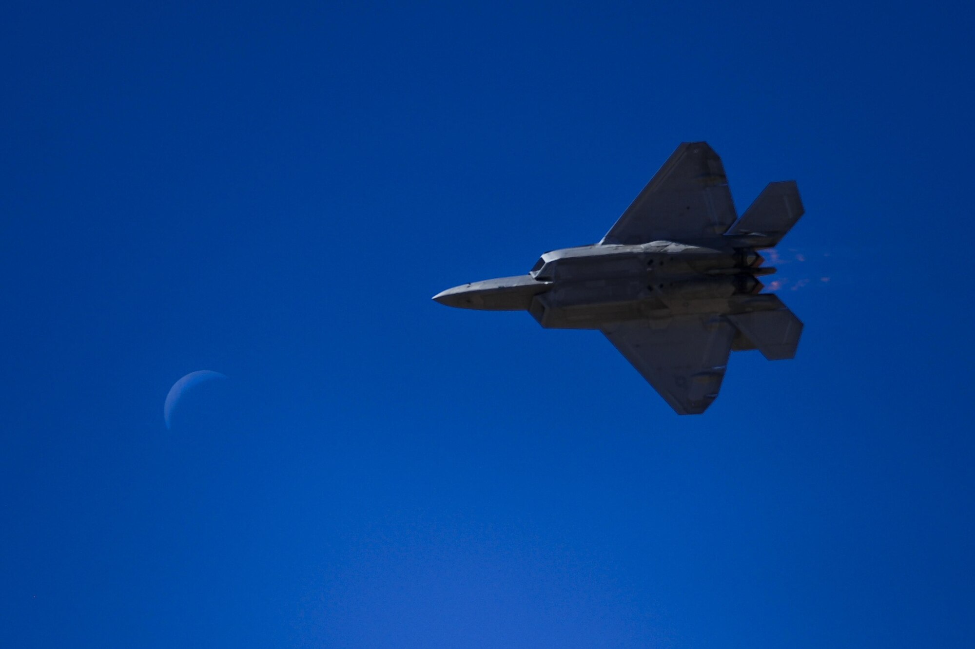 A U.S. Air Force F-22 Raptor flies in the foreground of the moon during the 2016 Heritage Flight Training and Certification Course at Davis-Monthan Air Force Base, Ariz., March 4, 2016. The annual aerial demonstration training event has been held at D-M since 2001, the course featured aerial demonstrations from historical and modern fighter aircraft. (U.S. Air Force photo by Senior Airman Chris Drzazgowski/Released) 