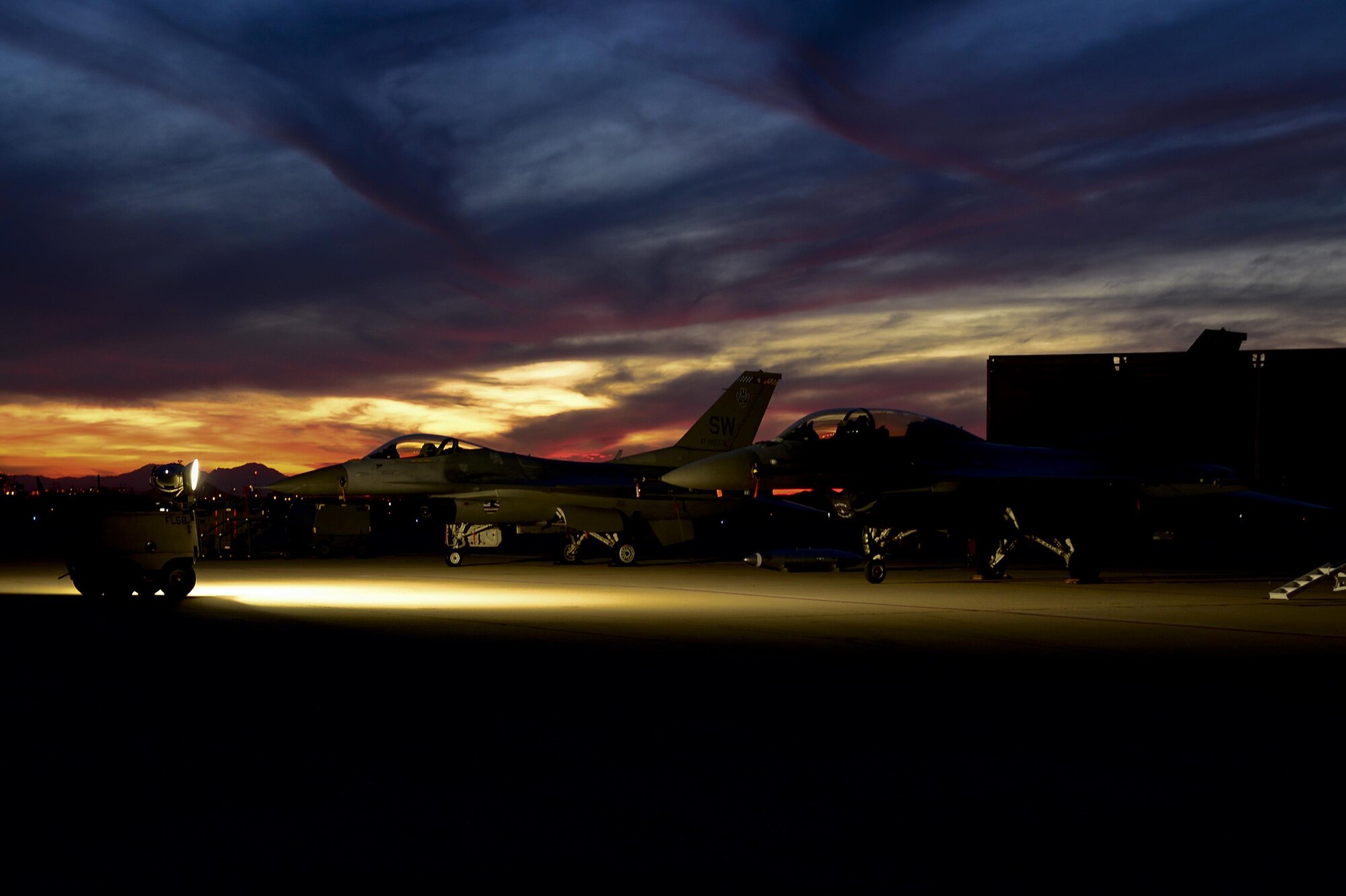 Two F-16D Fighting Falcons sit on the flightline during sunset after the first day of the 2016 Heritage Flight Training and Certification Course at Davis-Monthan Air Force Base, Ariz., March 4, 2016. The F-16D Fighting Falcon is a compact, multi-role fighter aircraft. It is highly maneuverable and has proven itself in air-to-air combat and air-to-surface attack. (U.S. Air Force photo by Senior Airman Chris Drzazgowski/Released)