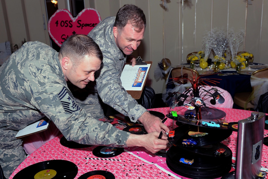 Chief MSgt. Shane Wagner (left), 4th Fighter Wing command chief, and Col. Mark Slocum (right), 4th Fighter Wing commander, inspect a table for the first-ever Spouses Dining-in, March 5, 2016, at Seymour Johnson Air Force Base, North Carolina. Approximately 100 people attended the dining-in dressed as characters from the movie theme of their squadron’s table. (U.S. photo/Airman 1st Class Ashley Williamson)