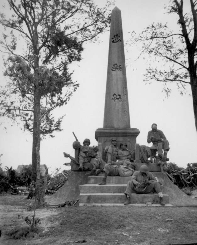 Marines, following the rapid Japanese retreat northward on Okinawa, pause for a moment's rest at the base of a Japanese war memorial during the Battle of Okinawa, April 12, 1945. They are (on steps) Pfc. F. O. Snowden; Navy Pharmacist's Mate, 2nd class R. Martin; (on monument, left to right) Pvt. J. T. Walton, Pvt. R. T. Ellenberg, Pfc. Clyde Brown, Pvt. Robb Brawner. (U.S. Marine Corps photo by Cpl. Art Sarno/Released)