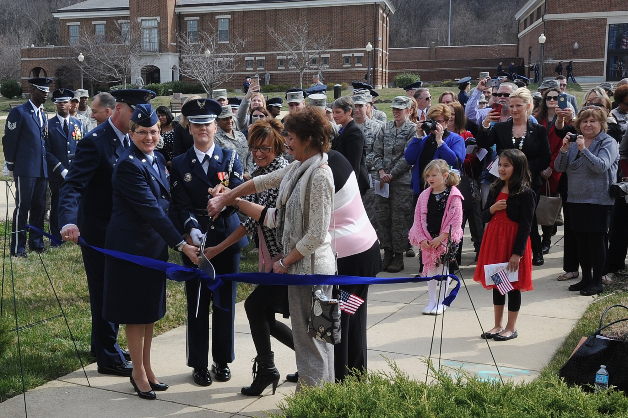 Four of the five first female Honor Guard members, Lt. Col. Cindi Feldwisch, Madelyn Ritz, Master Sgt. (ret.) Margaret Jones, and Elizabeth Byer join current members of the Air Force Honor Guard to cut a ribbon marking the unveiling of a new display case at the Honor Guard headquarters building, documenting the experience of the first female ceremonial guardsmen with pictures, mementos, and uniforms. The ribbon-cutting was part of a larger event honoring the first women to join the Air Force Honor Guard, Mar. 8. (U.S. Air Force photo/Jim Lotz)