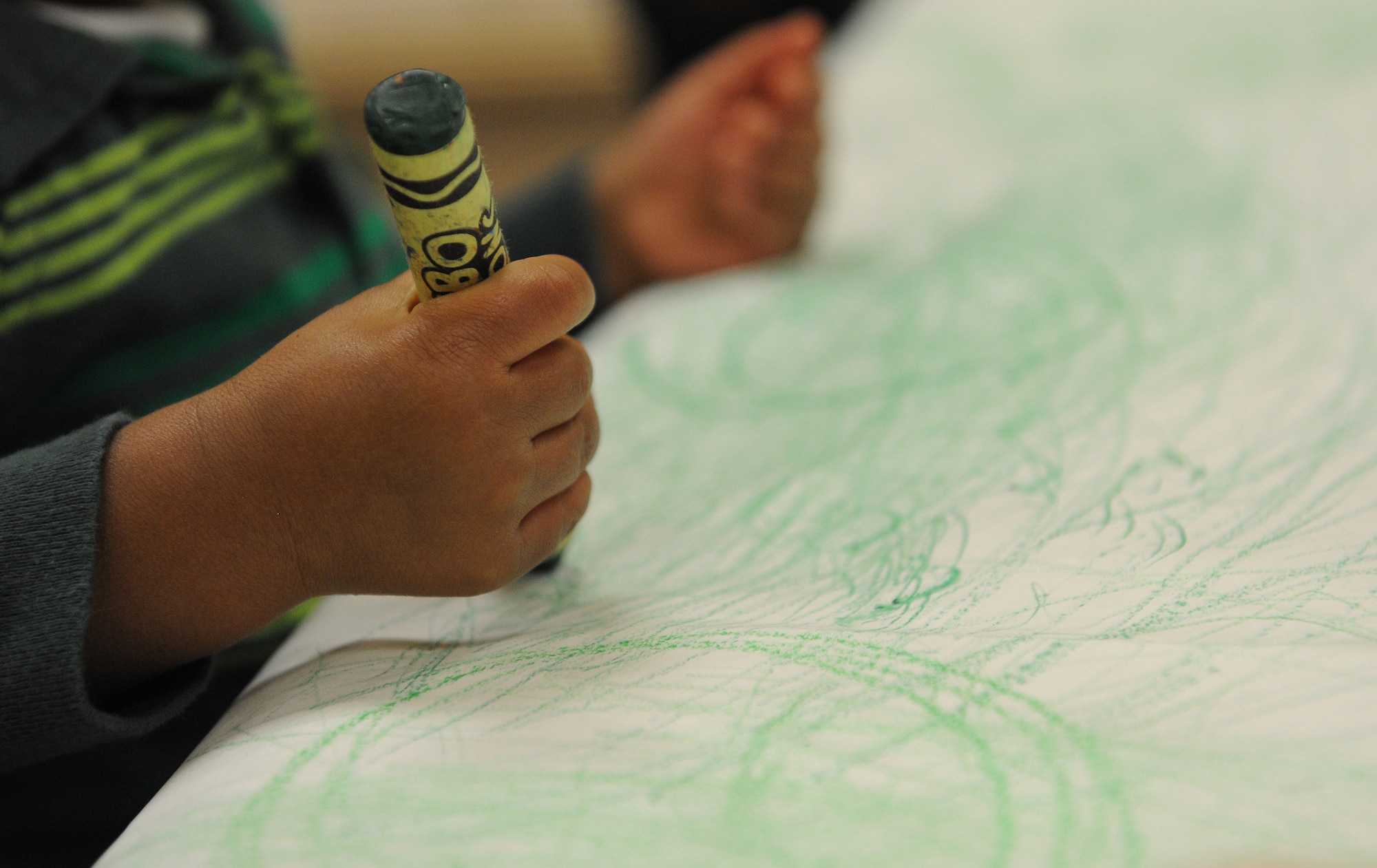 A young child draws with a green crayon after listening to the book Green Eggs and Ham by Dr. Seuss. This type of extended learning and creativity is a benefit of strong literacy programs and it has the potential to start early in a child’s development. (U.S. Air Force photos) 