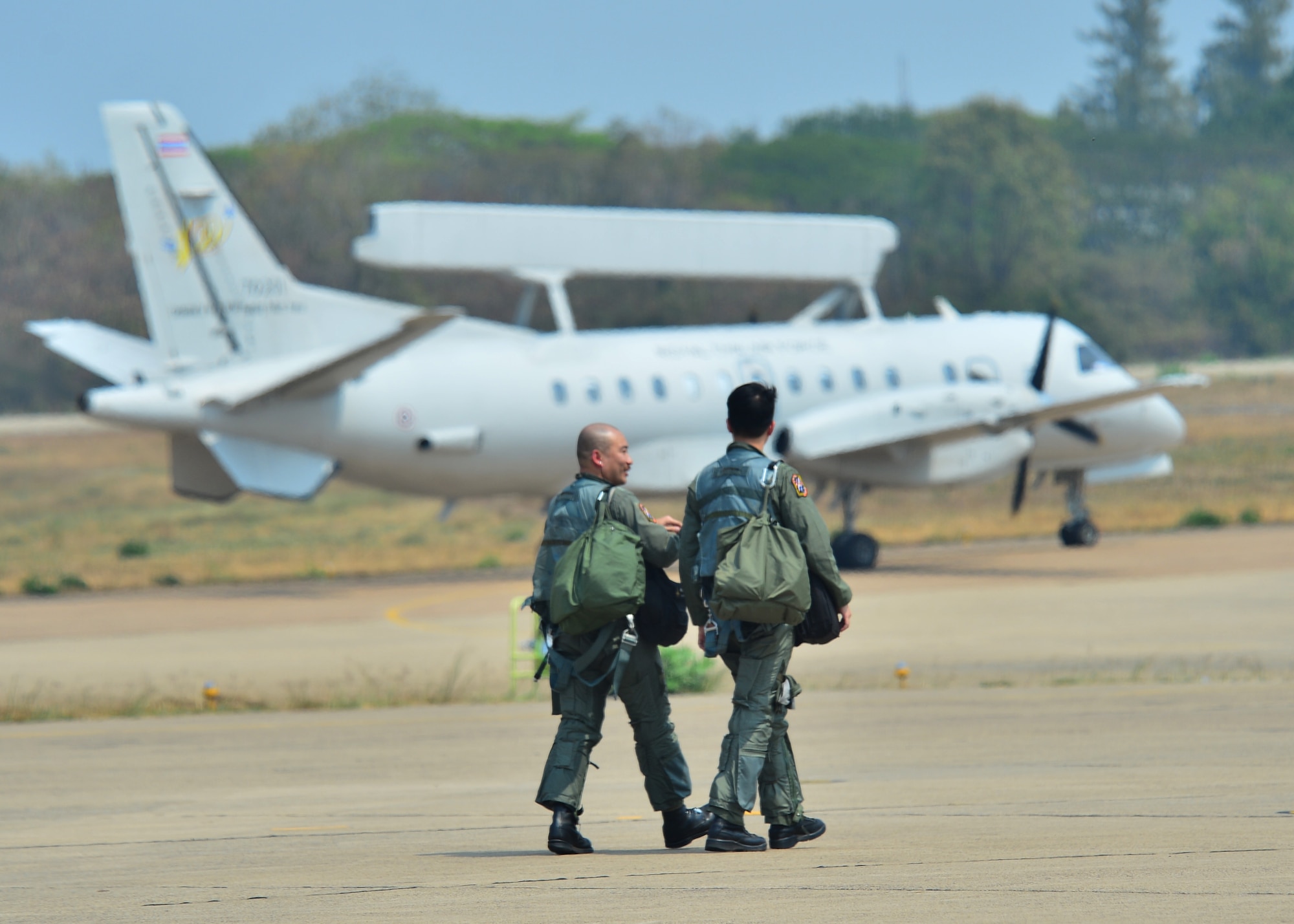 Two Republic of Singapore Air Force pilots walk and talk as a Royal Thai Air Force SAAB 340 AEW taxies past during Exercise Cope Tiger 16, on Korat Royal Thai Air Force Base, Thailand, March 7, 2016. Exercise Cope Tiger 16 includes over 1,200 personnel from three countries and continues the growth of strong, interoperable and beneficial relationships within the Asia-Pacific Region, while demonstrating U.S. capability to project forces strategically in a combined, joint environment. (U.S. Air Force Photo by Tech Sgt. Aaron Oelrich/Released)