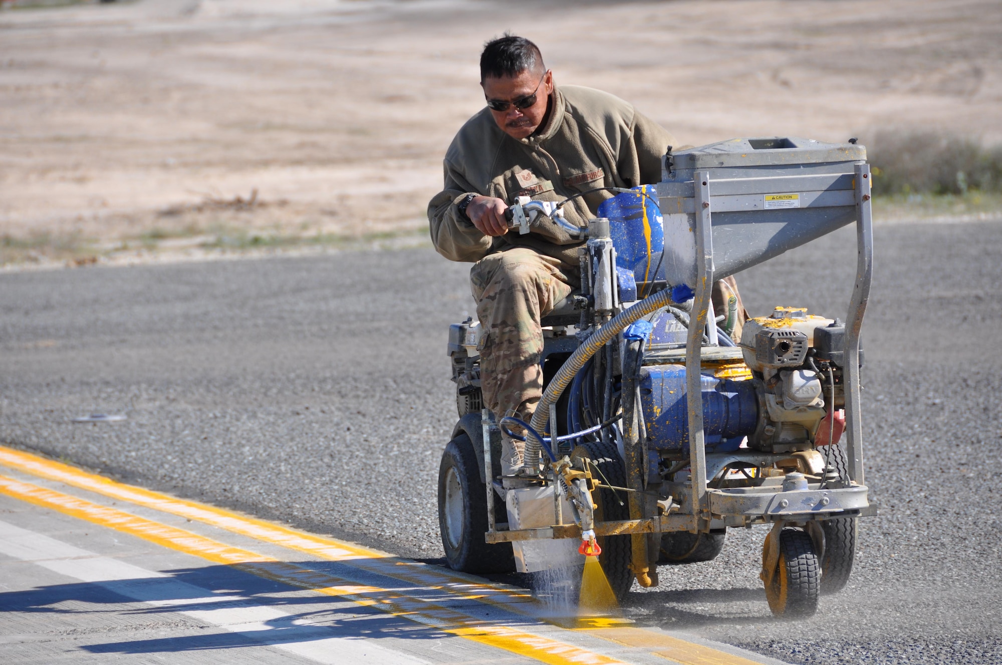 Tech. Sgt. Raymond Gipaya , 1st Expeditionary Civil Engineers Group, applies paint lines to a newly repaved aircraft parking surface at an undisclosed location in Southwest Asia, January 3, 2016.  Members of the 557th Expeditionary Civil Engineers Group, Red Horse, completed the asphalt repaving while members of the 1st ECEG Traveling Paint Team painted the lines.  (U.S. Air Force photo by Master Sgt. Kevin Nichols)
