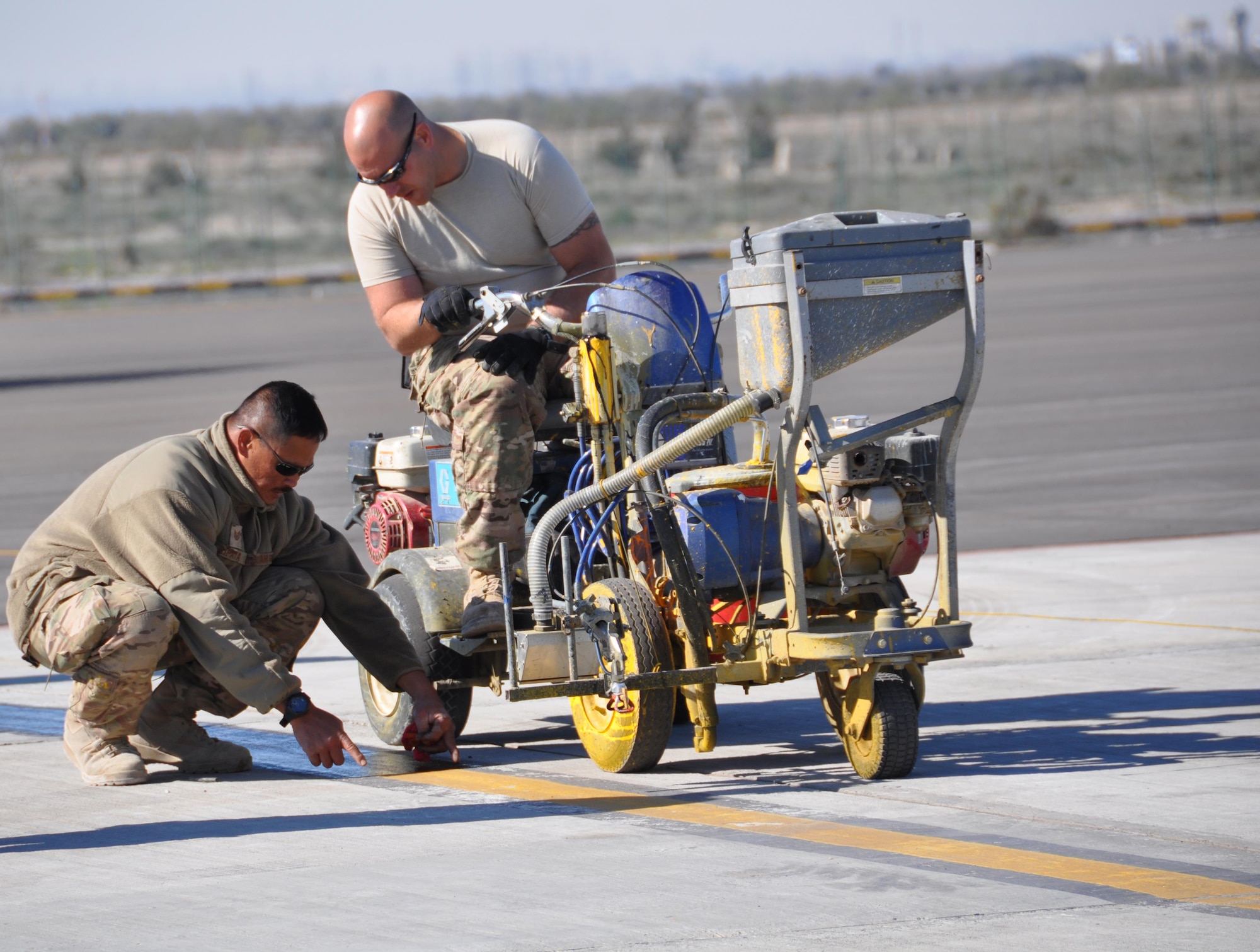 Tech. Sgt. Raymond Gipaya and Staff Sgt. Travis Bowersock, 1st Expeditionary Civil Engineers Group, apply paint lines to a newly repaved aircraft parking surface at an undisclosed location in Southwest Asia, January 3, 2016.  Members of the 557th Expeditionary Civil Engineers Group, Red Horse, completed the asphalt repaving while members of the 1st ECEG Traveling Paint Team painted the lines. (U.S. Air Force photo by Master Sgt. Kevin Nichols) 