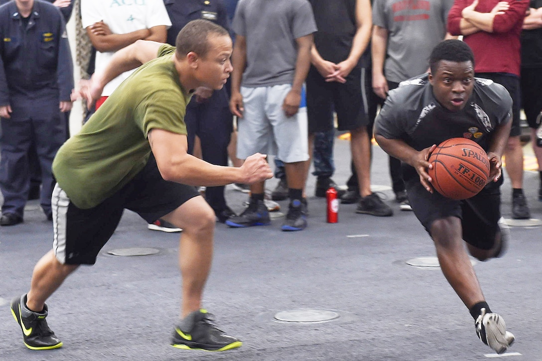 Navy Petty Officer 2nd Class DaMario MacFrasier dribbles the ball past Petty Officer 1st Class Brandon Sledge during a divisional March Madness basketball tournament aboard the amphibious transport dock ship USS Arlington in the Arabian Gulf, March 5, 2016. The Arlington is supporting maritime security operations and theater security cooperation efforts in the U.S. 5th Fleet area of operations. Navy photo by Petty Officer 3rd Class Kaleb R. Staples