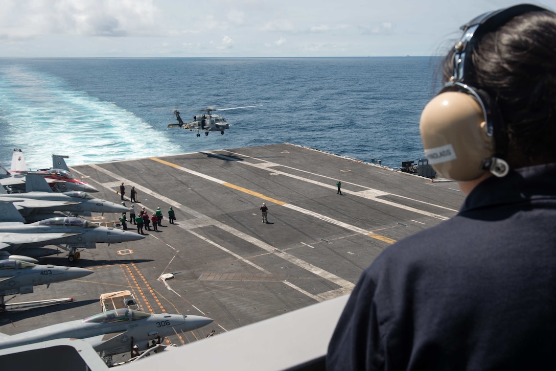 Navy Seaman Katlynn Joe stands lookout on the superstructure of the aircraft carrier USS John C. Stennis as an MH-60R Sea Hawk helicopter assigned to the Raptors of Helicopter Maritime Strike Squadron 71 lands on the ship's flight deck in the South China Sea, March 6, 2016. Navy photo by Petty Officer 2nd Class Jonathan Jiang