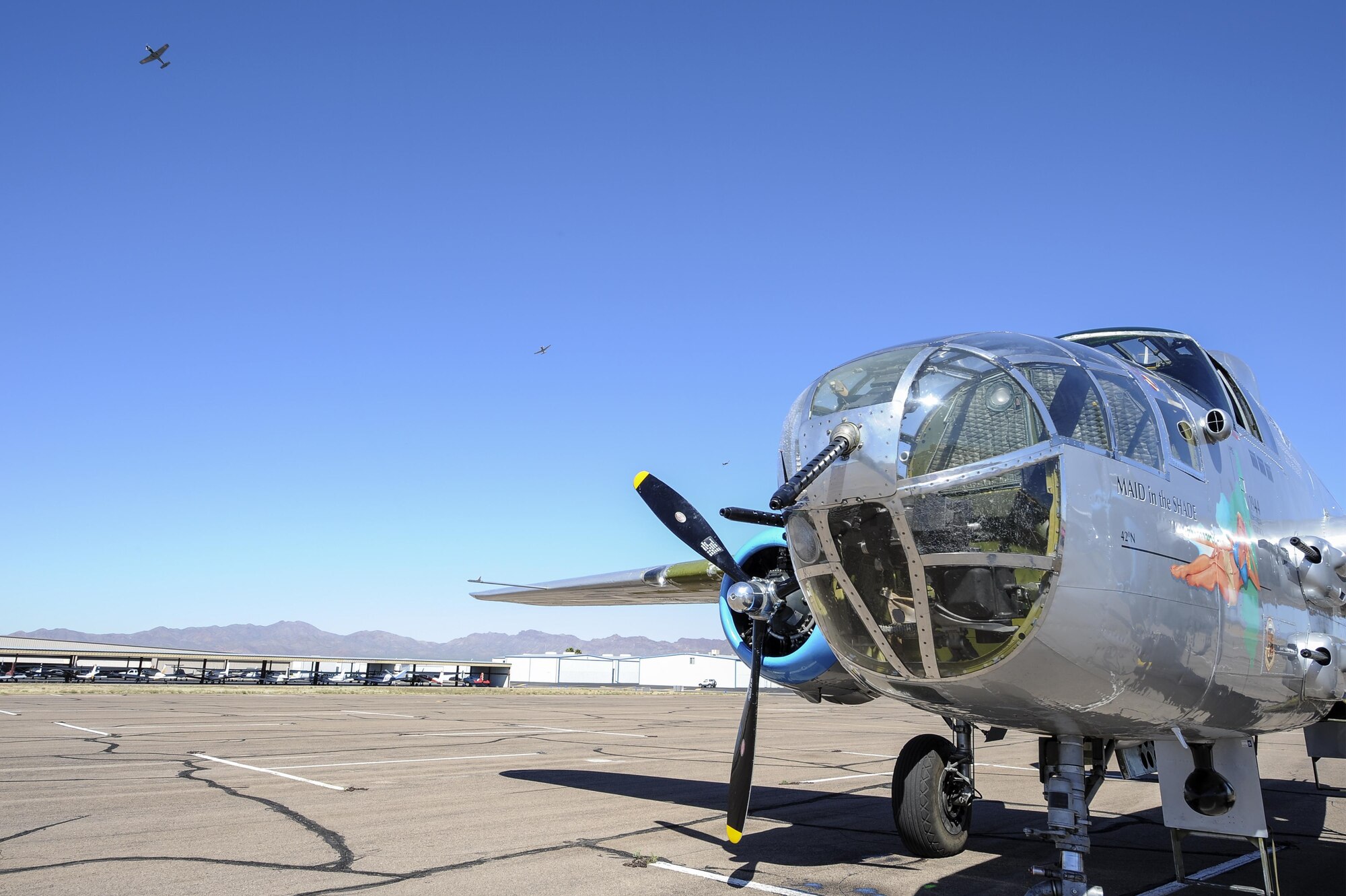 A North American B-25 Mitchell sits on the flightline while three CJ-6 Desert Rats fly in formation at the Ryan Airfield in Tucson, Ariz., March 10, 2016. The B-25 and CJ-6s will be performing at the upcoming Thunder and Lightning over Arizona Open House. (U.S. Air Force photo by Airman 1st Class Mya M. Crosby/Released)