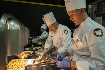 U.S. Army Reserve Culinary Arts Team members Staff Joseph Parker, center, and Staff Sgt. Jeffery Vaughn, plate the first course during the Military Hot Food Kitchen category at the 41st Annual Military Culinary Arts Competitive Training Event, March 10, 2016, at Fort Lee, Va.. The team prepared Roasted Golden and Burgundy Beet Salad, Coq au Vin Nuevo (Chicken braised in red wine), and Molten Lava Cake working on a Mobile Kitchen Trailer for 45 dining guests. (U.S. Army photo by Timothy L. Hale) (Released)