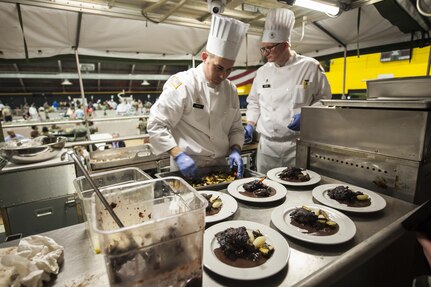 U.S. Army Reserve Culinary Arts Team captain, Staff Joseph Parker, left, and team manager, Chief Warrant Officer 2 Colby Beard, plate the main course during the Military Hot Food Kitchen category at the 41st Annual Military Culinary Arts Competitive Training Event, March 10, 2016, at Fort Lee, Va.. The team prepared Roasted Golden and Burgundy Beet Salad, Coq au Vin Nuevo (Chicken braised in red wine), and Molten Lava Cake working on a Mobile Kitchen Trailer for 45 dining guests. (U.S. Army photo by Timothy L. Hale) (Released)