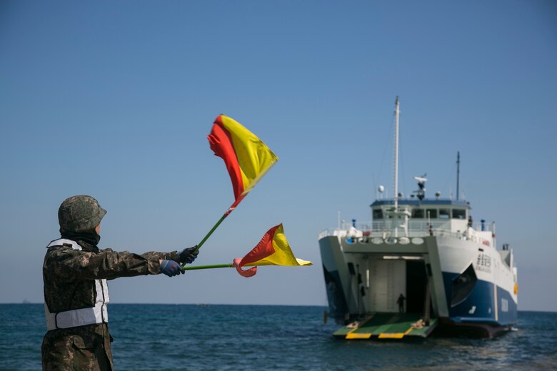 A Republic of Korea Marine waves flags for a Korean ship to land prior to an amphibious assault rehearsal at Doksukri Beach, ROK, March 11, 2016, during Ssang Yong 16. Ssang Yong is a biennial military exercise focused on strengthening the amphibious landing capabilities of the ROK, the U.S., New Zealand and Australia. (U.S. Marine Corps photo by MCIPAC Combat Camera Cpl. Allison Lotz/Released)