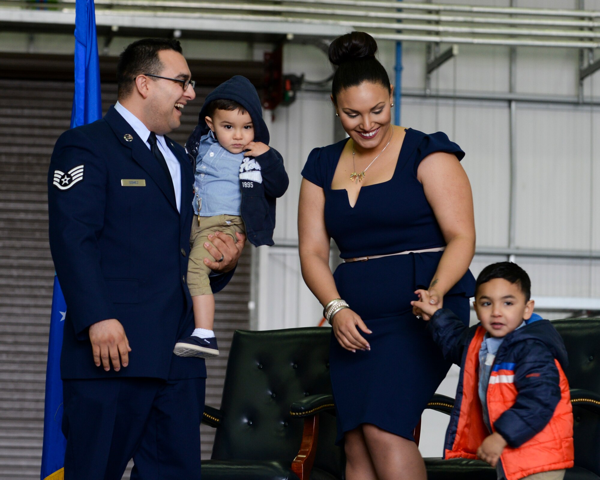 U.S. Air Force Staff Sgt. Vicente Gomez, 100th Aircraft Maintenance Squadron crew chief, left, assists his wife and children on stage during a ceremony March 11, 2016, on RAF Mildenhall, England. Gomez was presented with the Airman’s Medal for voluntary risk of life near RAF Mildenhall on May 12, 2014. By quickly assessing a catastrophic scene, Gomez was able to render lifesaving assistance to two victims of a potentially fatal car accident.  (U.S. Air Force photo by Senior Airman Victoria H. Taylor/Released)