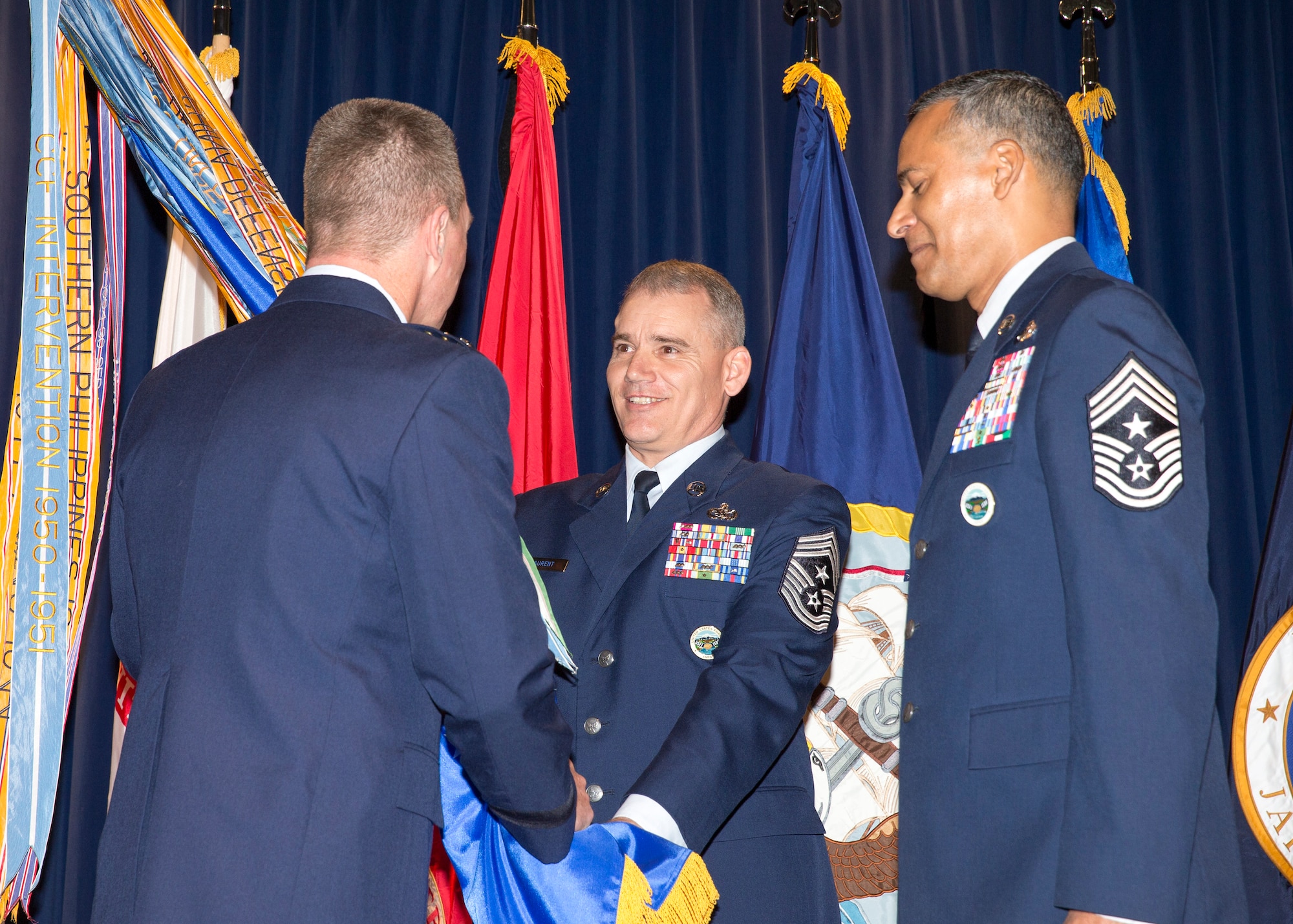 Chief Master Sgt. James Laurent, U.S. Forces Japan and 5th Air Force outgoing command chief, passes the 5th AF guideon to Lt. Gen. John Dolan, USFJ and 5th AF commander while Chief Master Sgt. Terrrence Greene, USFJ and 5th AF incoming command chief, stands by to receive it at Yokota Air Base, Japan, March 10, 2016. Laurent was the communications link between the commander and the enlisted community. (U.S. Air Force photo by Yasuo Osakabe/Released)
