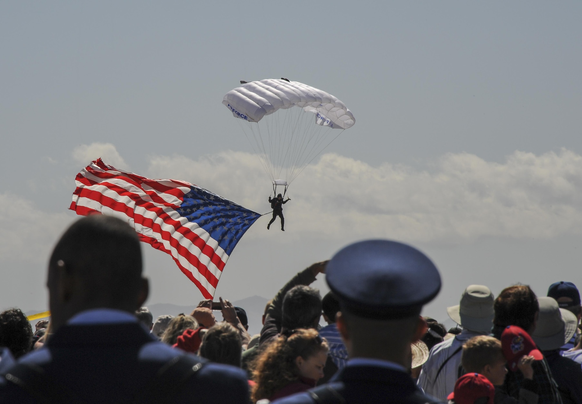 Spectators watch as U.S. Air Force Master Sgt. James Cane, U.S Air Force Skydiving Team, Wings of Blue, lands with the American flag during Thunder and Lightning over Arizona Open House at Davis-Monthan Air Force Base, Ariz., March 12, 2016. The Wings of Blue Demonstration Team travels across the country to events represent the Air Force in precision parachuting. (U.S. Air Force photo by Airman 1st Class Mya M. Crosby/Released)
