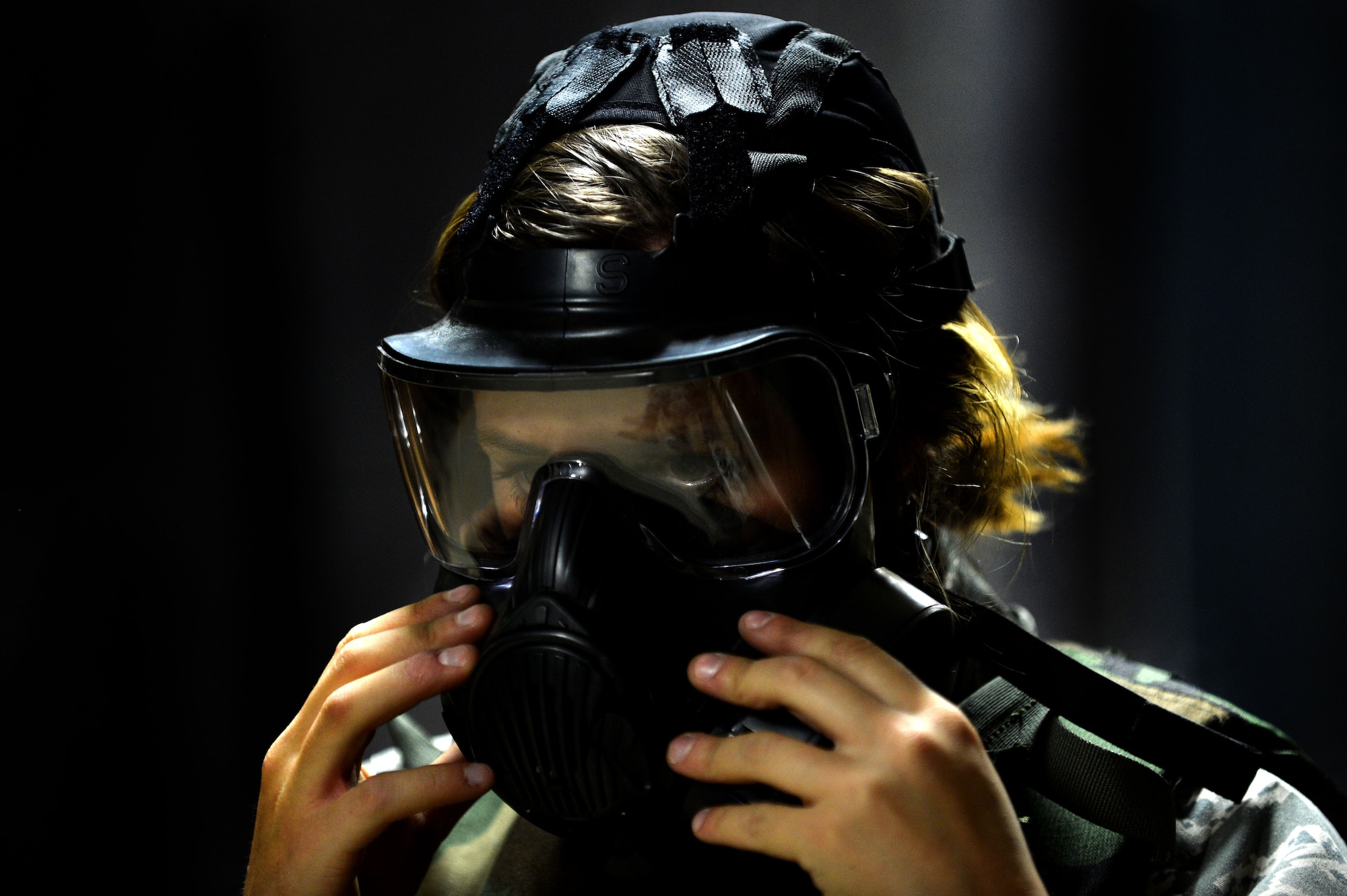 A U.S. Airman puts on her gas mask before firing the M4 carbine during combat arms training at Shaw Air Force Base, S.C., March 8, 2016. During the weapons qualification portion of CATM, students have to shoot their weapons from the prone, kneeling, standing positions, and at times with a gas mask to ensure they are capable of firing from all positions. (U.S. Air Force photo by Senior Airman Michael Cossaboom)