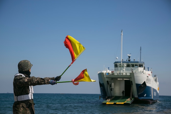 A Republic of Korea Marine waves flags for a Korean ship to land prior to an amphibious assault rehearsal at Doksukri Beach, ROK, March 11, 2016, during Ssang Yong 16. Ssang Yong is a biennial military exercise focused on strengthening the amphibious landing capabilities of the ROK, the U.S., New Zealand and Australia. (U.S. Marine Corps photo by Cpl. Allison Lotz/Released)